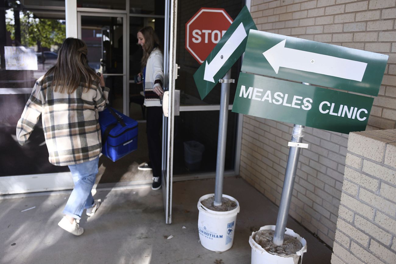 Someone walking into a health department. There's a green sign that says "Measles Clinic."